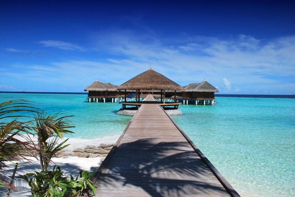 Luxury overwater bungalow with wooden jetty extending into crystal-clear turquoise lagoon at tropical beach resort
