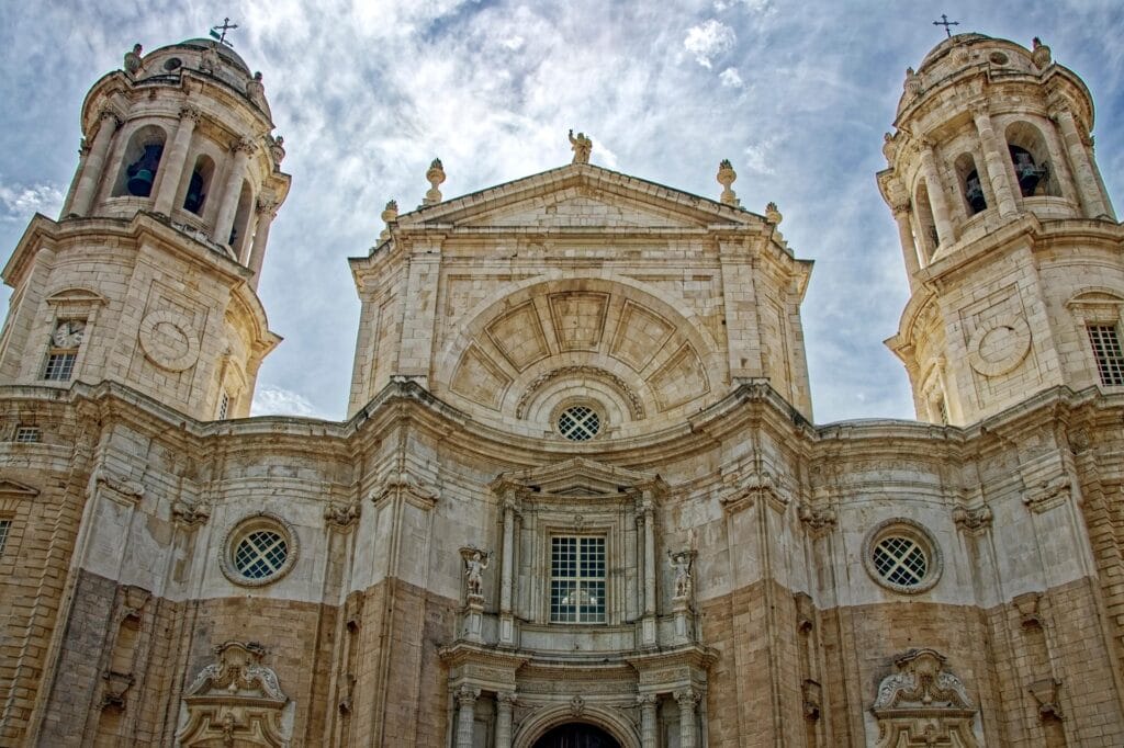 Historic Cádiz cathedral with golden dome overlooking Atlantic coastline at sunset, narrow cobblestone streets with traditional architecture visible
