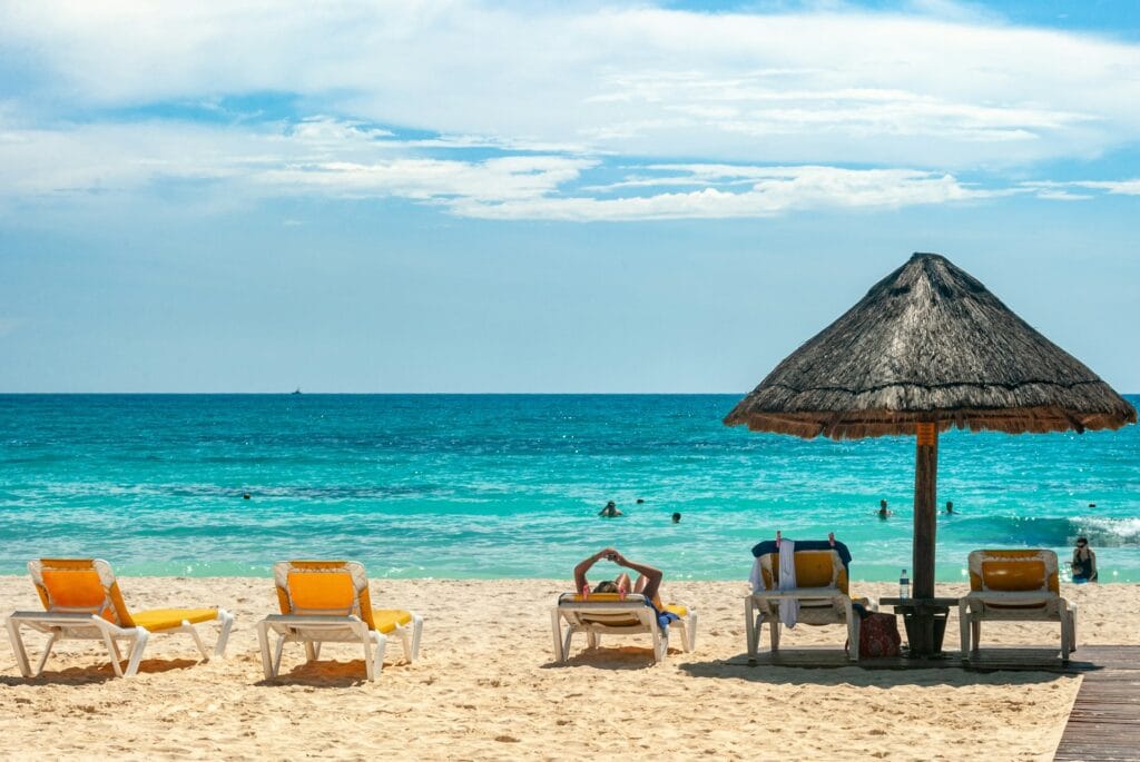 Brown beach umbrellas and lounge chairs on pristine sandy Caribbean beach with turquoise ocean water

