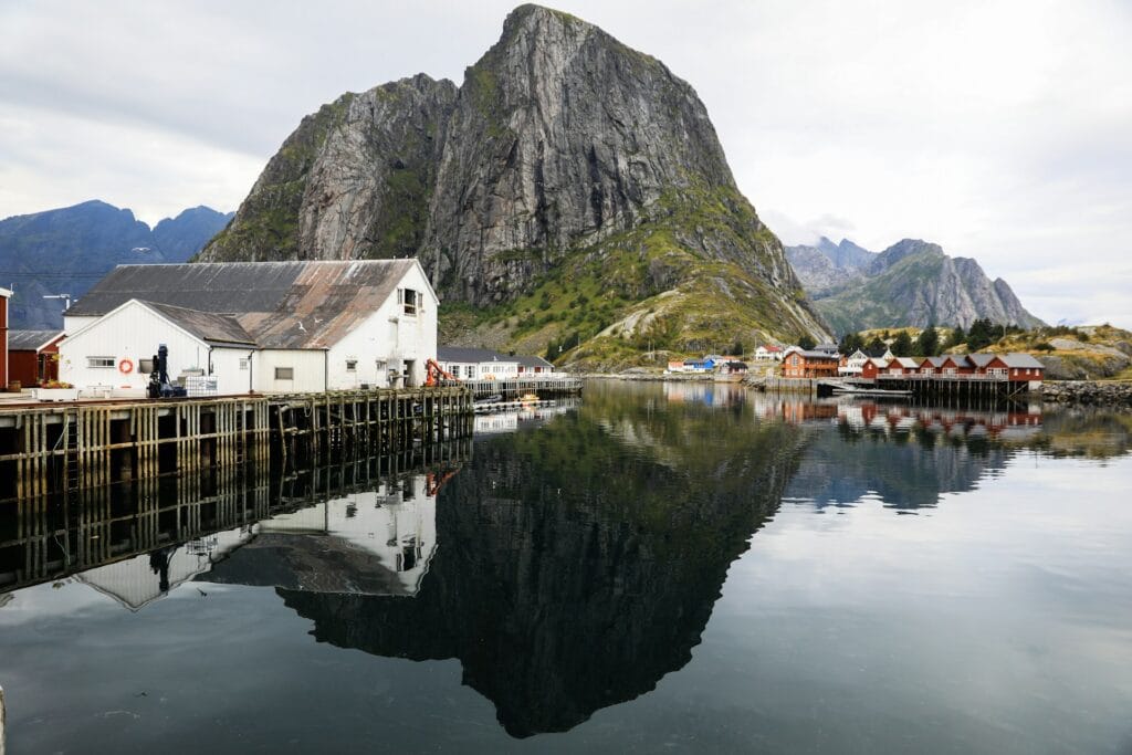Traditional red rorbuer fishing cabins in Reine with sharp Lofoten peaks rising behind calm water