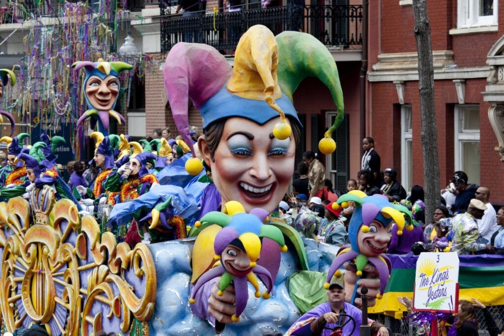 New Orleans Mardi Gras parade float decorated with colorful themes, beaded necklaces visible, costumed riders, crowds in French Quarter street