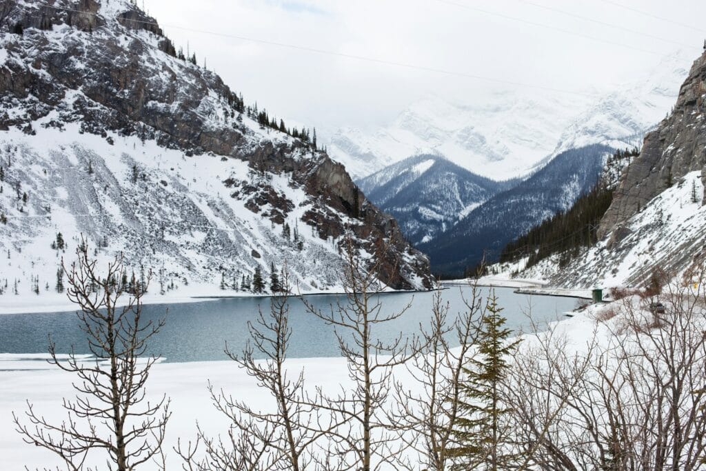 Frozen Lake Louise with mirror-like ice surface reflecting snow-covered Canadian Rocky Mountains, log cabin on shore, sunset light over peaks