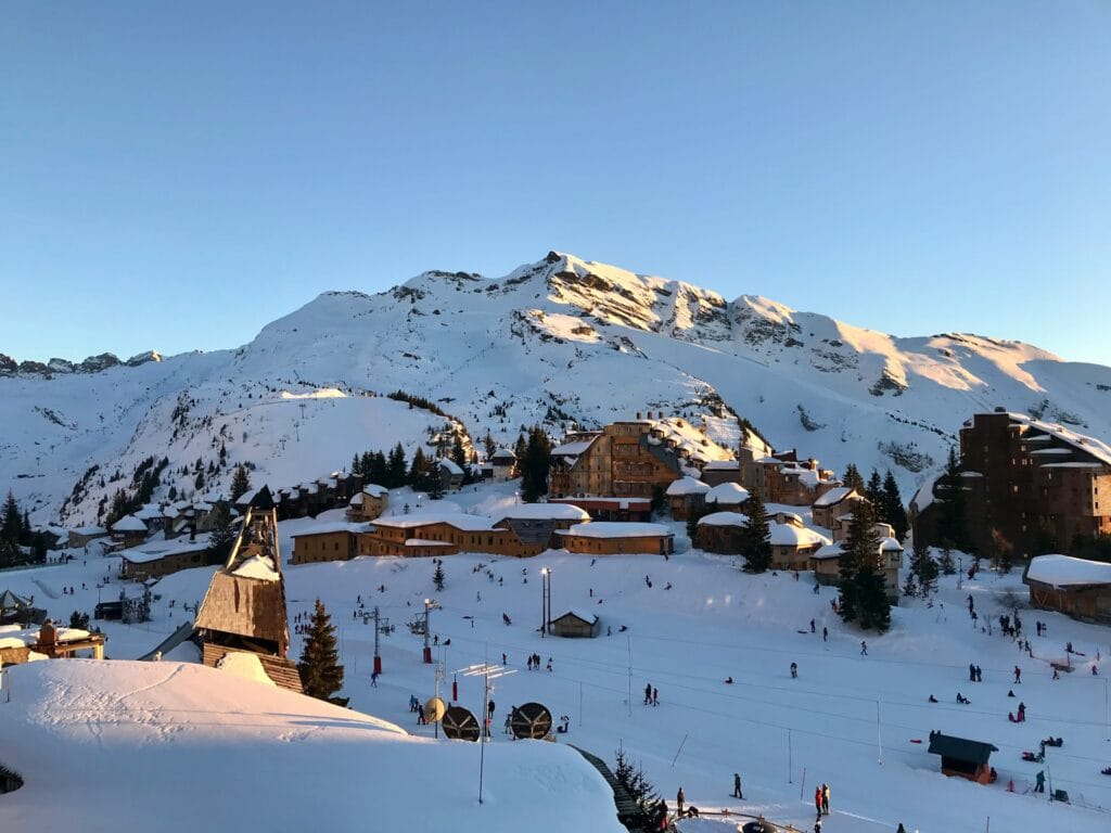 Wide view of a ski resort with groomed slopes, ski lifts, snow-covered mountains, and skiers enjoying powder runs down the mountainside