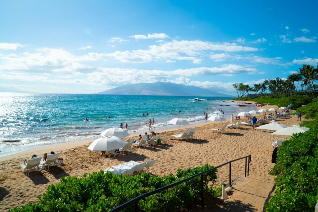 Hawaii beach filled with white umbrellas and families in the water, tropical paradise setting for summer vacation