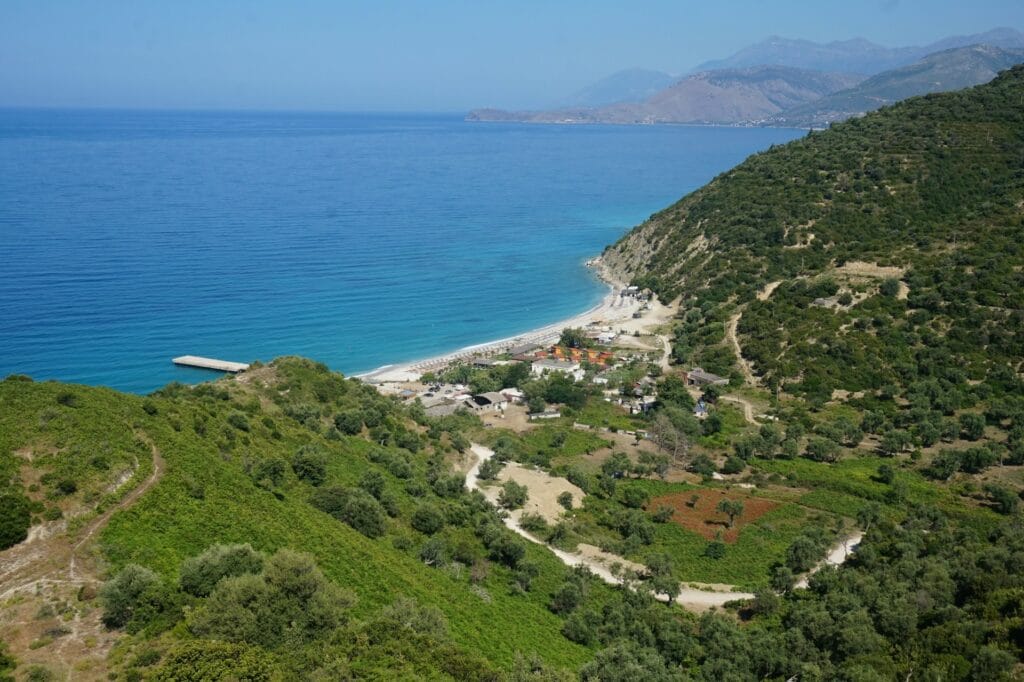 Albanian Riviera turquoise water with rocky coastline cliffs and small beach cove, budget Mediterranean vacation destination