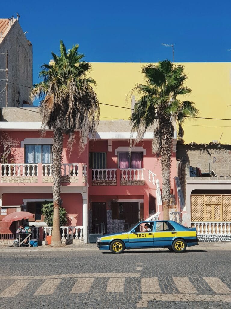Colorful blue and yellow taxi parked on Cape Verde street with tall palm tree, showing the vibrant local character and tropical island lifestyle