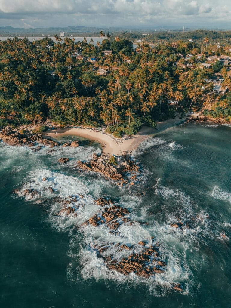 Aerial overhead shot of Mirissa Beach in Sri Lanka showing pristine turquoise water, white sand beach, palm trees, and traditional fishing boats