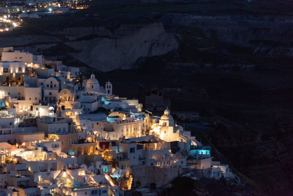Santorini Greece aerial view at night with glowing golden lights reflecting off white buildings and Caldera, Mediterranean Sea, island landscape