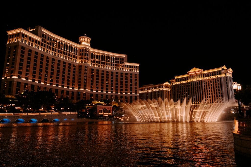 Bellagio fountain show at night with illuminated water jets and Las Vegas Strip lights in background
