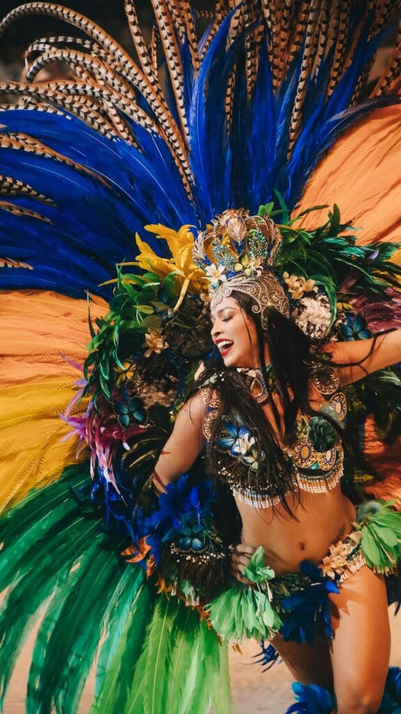 Woman wearing elaborate Carnival costume with colorful feathered headdress, sequined top, and festive celebration makeup during Rio Carnival