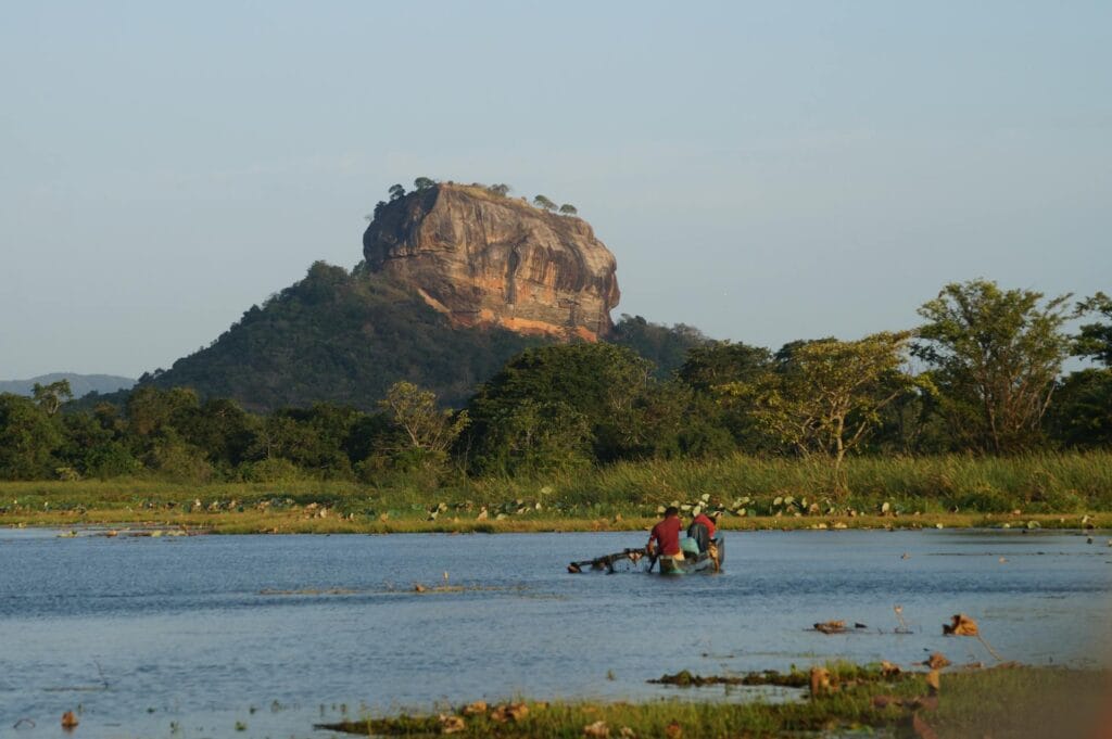 Ancient Sigiriya Rock fortress rising dramatically from lush green valley with terraced gardens and traditional Sri Lankan architecture visible