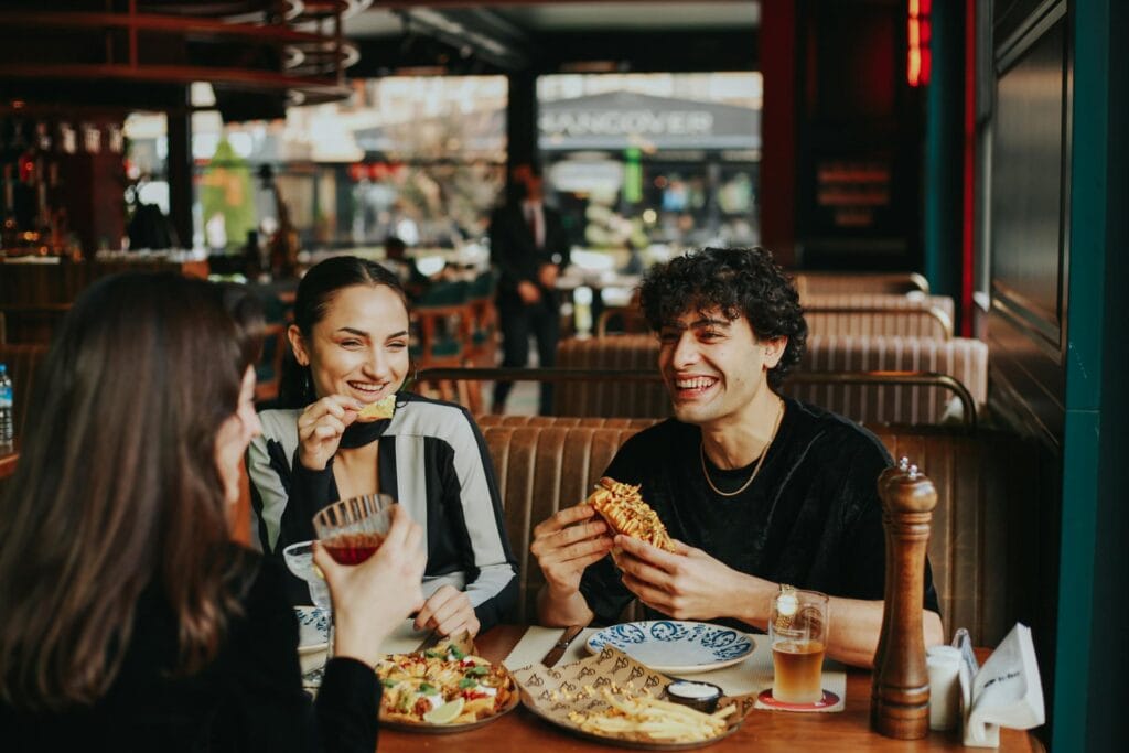 Diverse group of happy women eating pizza and socializing at a restaurant table, watching their drinks and enjoying food safety while traveling