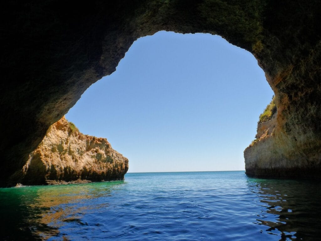 Algarve Portugal golden rocky sea cave grotto opening overlooking turquoise Mediterranean water, dramatic limestone cliffs