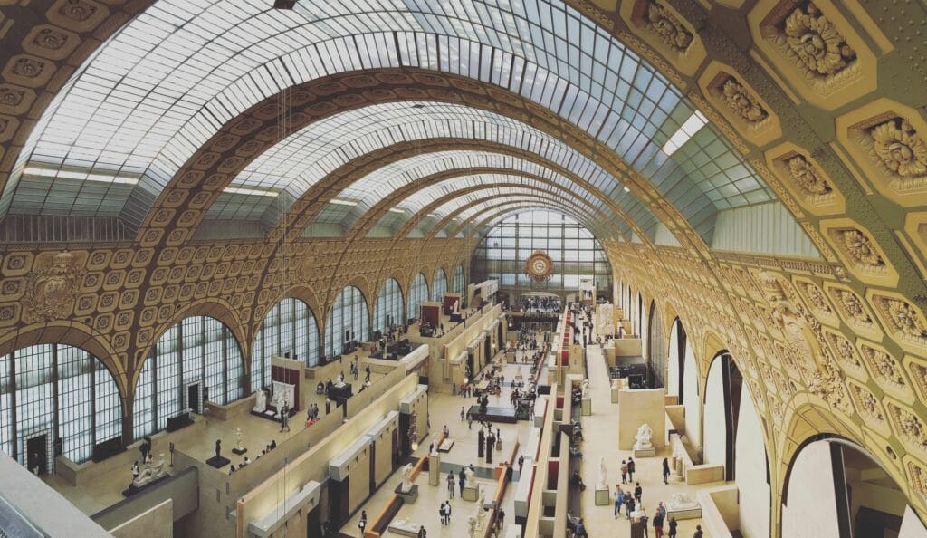 Musée d'Orsay interior with accessible ramps and elevators connecting all floors, wheelchair user viewing Impressionist artwork, accessibility features visible