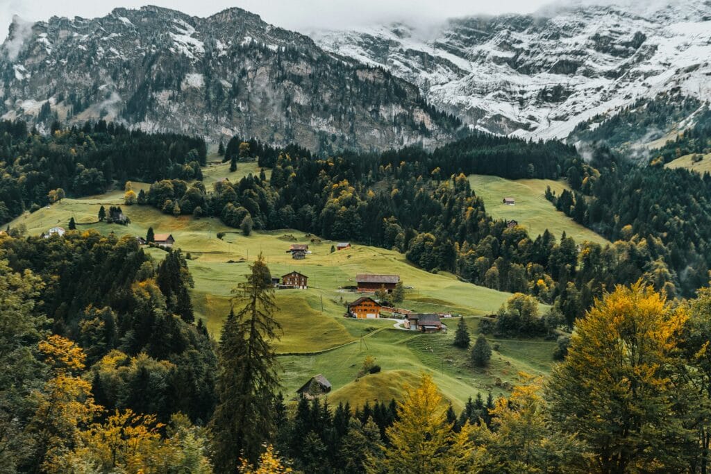 Aerial view of Swiss Alpine village with green pastures and traditional chalets, reflecting Switzerland's safe solo travel destination status"