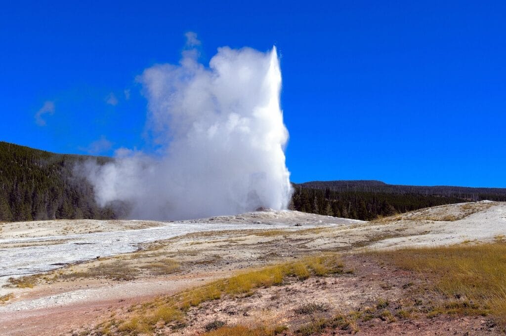 Yellowstone Old Faithful geyser erupting with crowds watching from designated area, geysers in background, family-friendly hiking trail