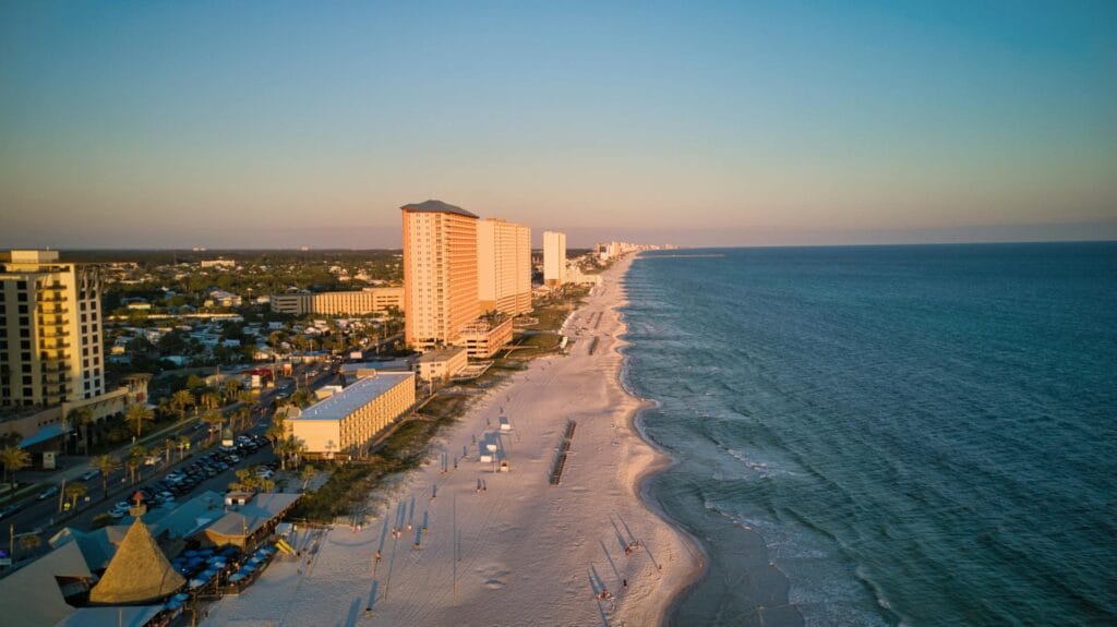 Aerial sunset view of the long white sand beach and coastal high-rise hotels in Panama City Beach, Florida