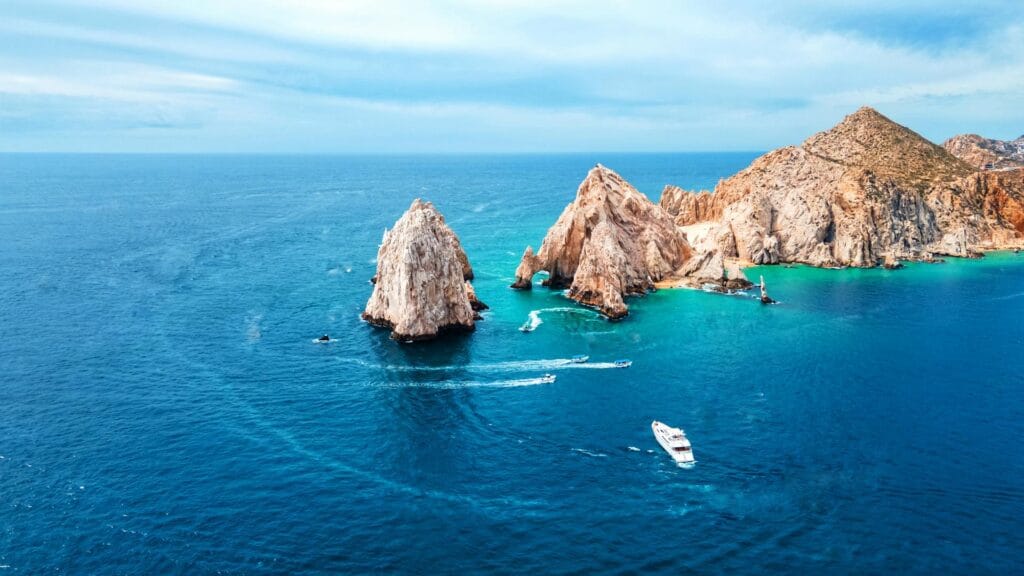 The iconic El Arco rock formation at Land's End in Cabo San Lucas, Mexico, with boats cruising the deep blue water.