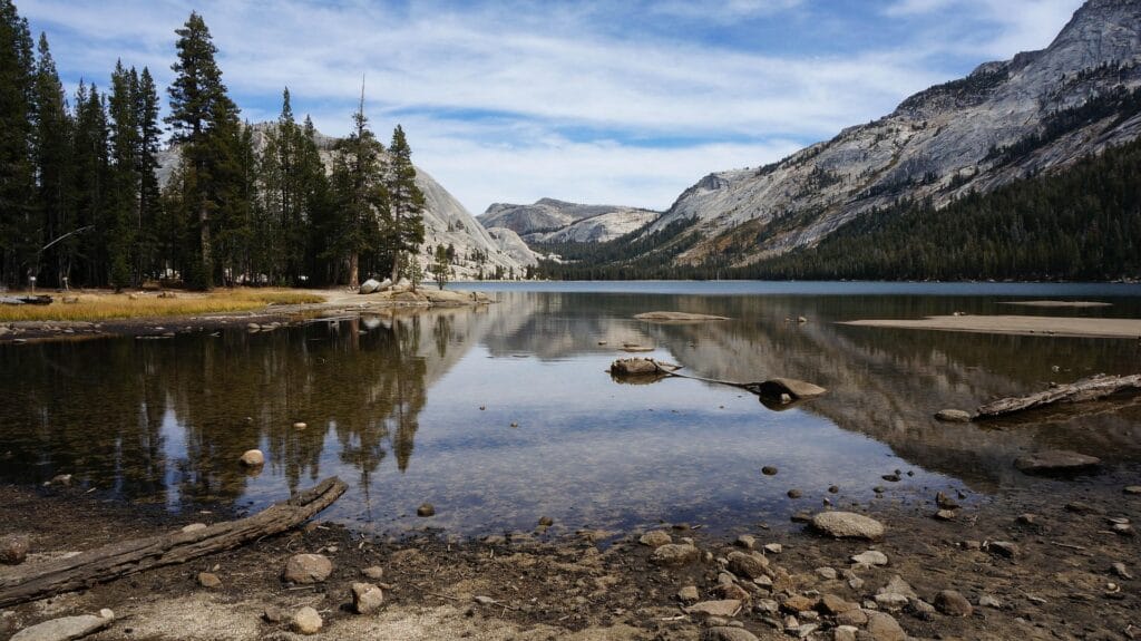 Reflection of granite mountains and pine trees in a calm, clear lake within Yosemite National Park.