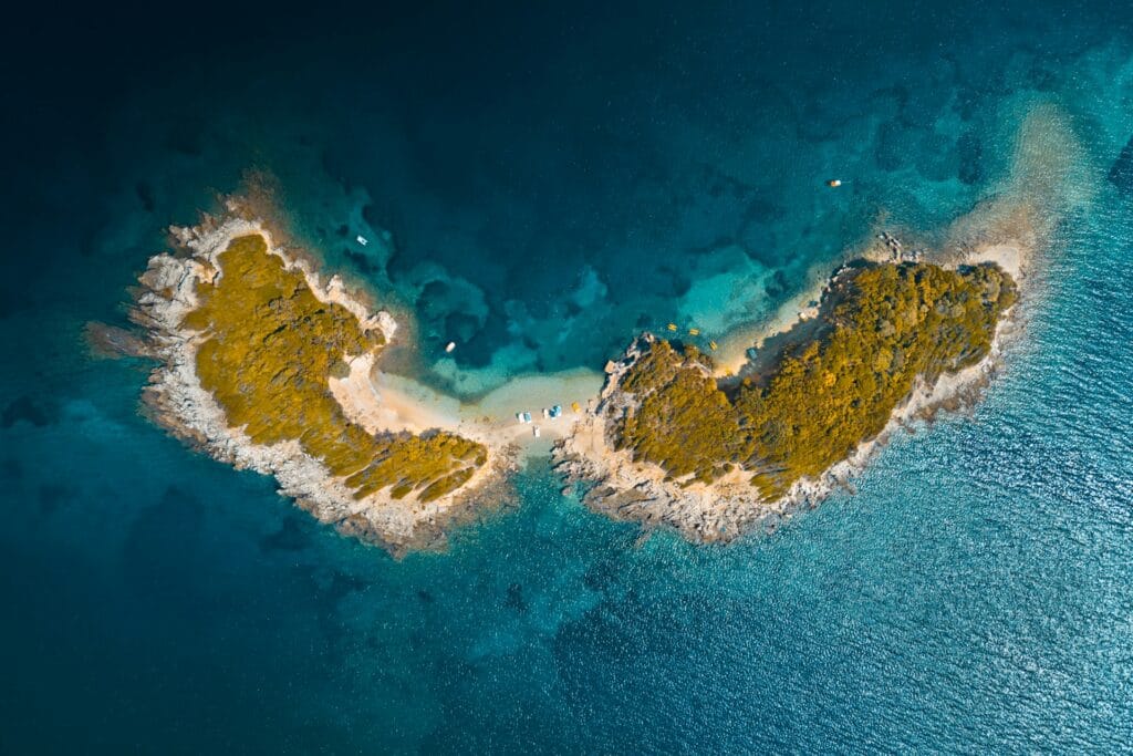Aerial view of a small turquoise bay with a sandy beach and lush greenery on the Albanian Riviera.