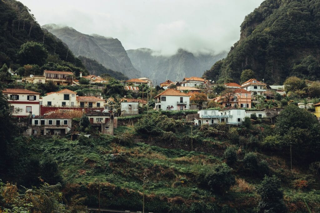 Traditional red-roofed houses nestled on a lush, green mountain slope in Madeira under a cloudy sky.
