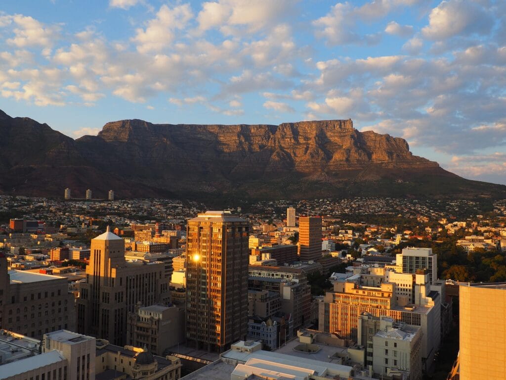A wide panoramic view of the Cape Town city skyline at sunset with the flat-topped Table Mountain in the background