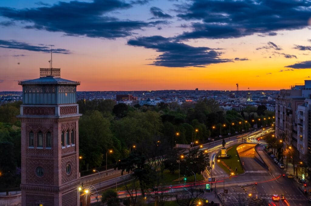 Evening sunset view of the Madrid city skyline in Spain, showcasing historical architecture and glowing street lights.