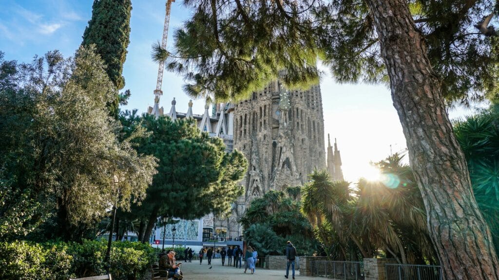 A group of people walking in the sun in front of the Sagrada Familia basilica in Barcelona.