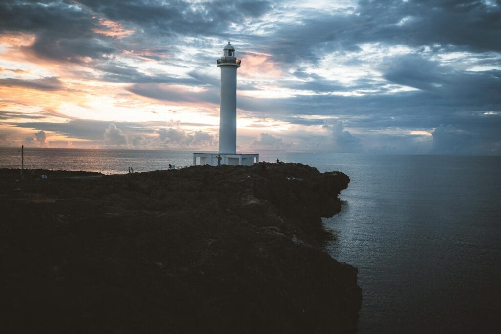 Scenic coastal landscape of Okinawa, Japan, featuring a lighthouse on a rocky cliff overlooking the blue ocean.