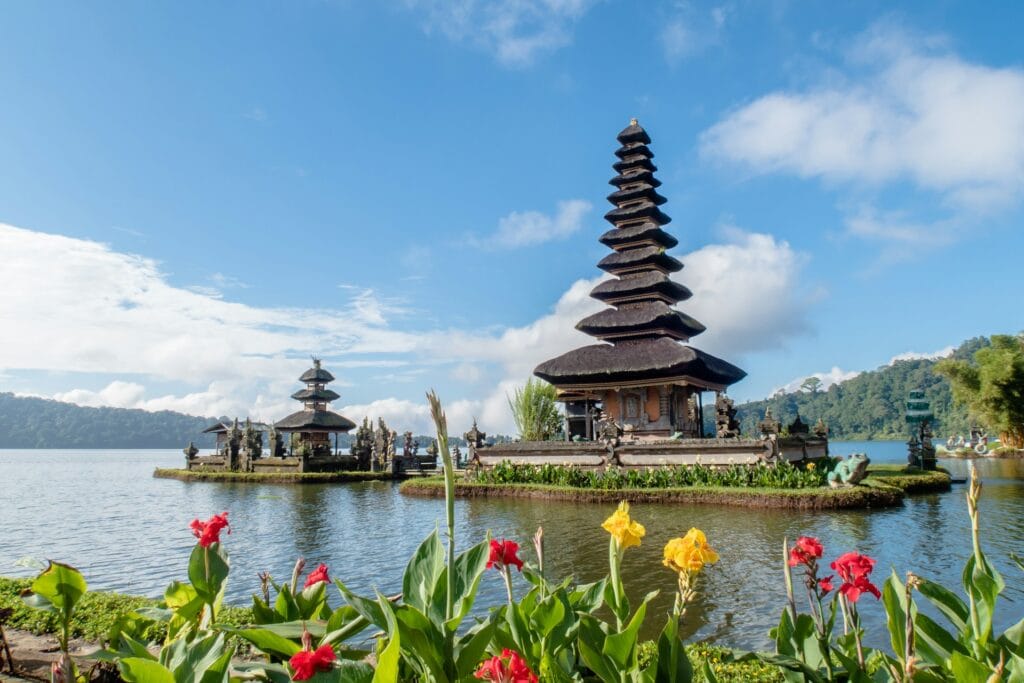 The Pura Ulun Danu Bratan water temple in Bali, Indonesia, situated on a calm lake with flowers and mountains in the background.