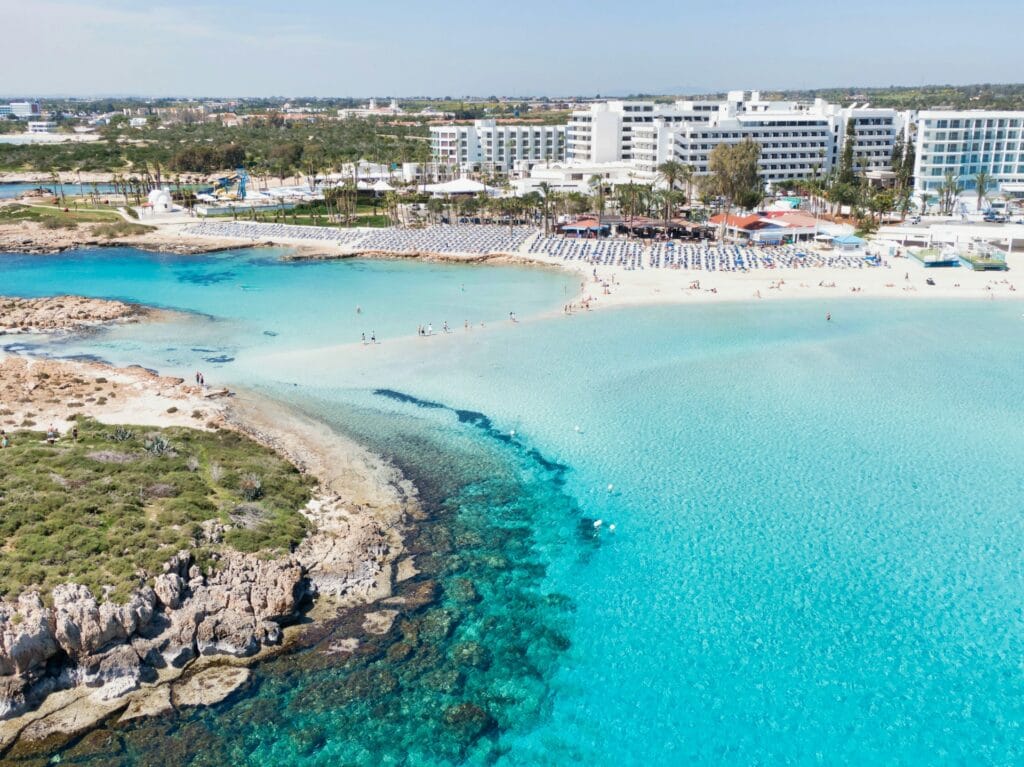 Aerial view of a white sand beach and turquoise water at a resort in Cyprus during a sunny April day.