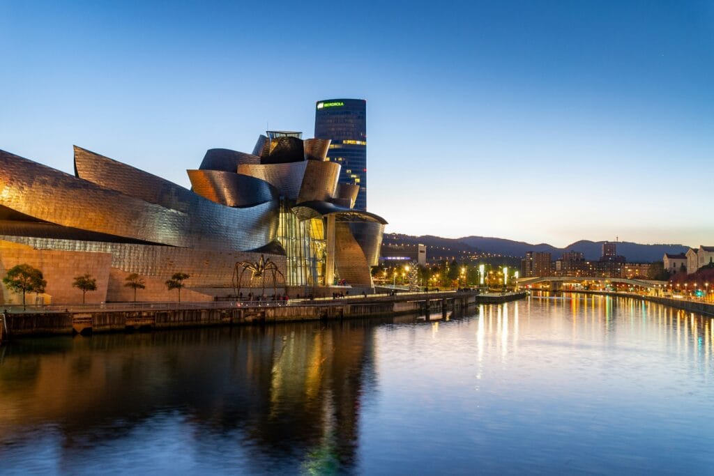 The futuristic titanium architecture of the Guggenheim Museum Bilbao sitting along the banks of the Nervión River in Spain.
