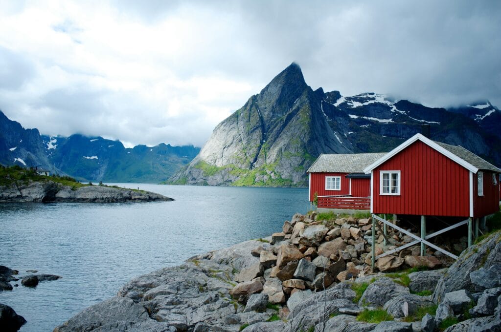 Traditional red and white wooden house situated on a rocky coast in front of a calm body of water in Norway.