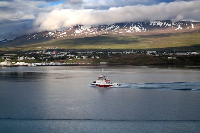 A lone boat sailing smoothly across the calm, atmospheric gray waters of the Eyjafjordur fjord near Akureyri, Iceland.