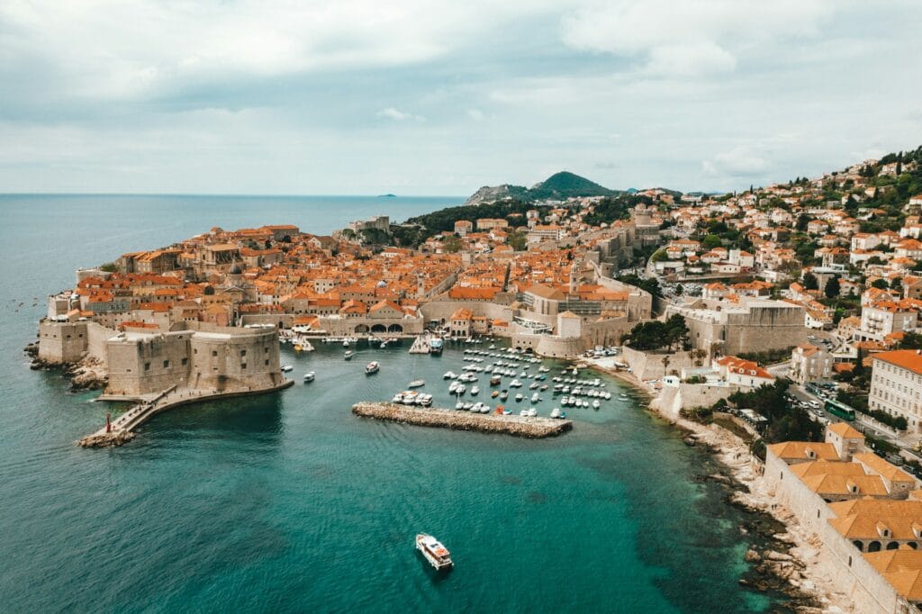 Aerial view of the orange-roofed medieval buildings and historic stone walls of Dubrovnik Old Town bounded by the Adriatic Sea.