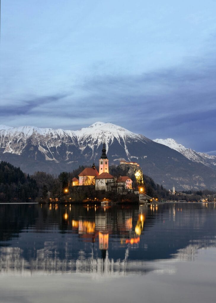 Lake Bled, Slovenia, featuring the iconic island church against a backdrop of snow-capped mountains at dusk