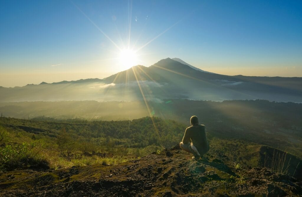 A hiker looking out over a misty volcanic landscape from a mountain peak in Bali at sunrise