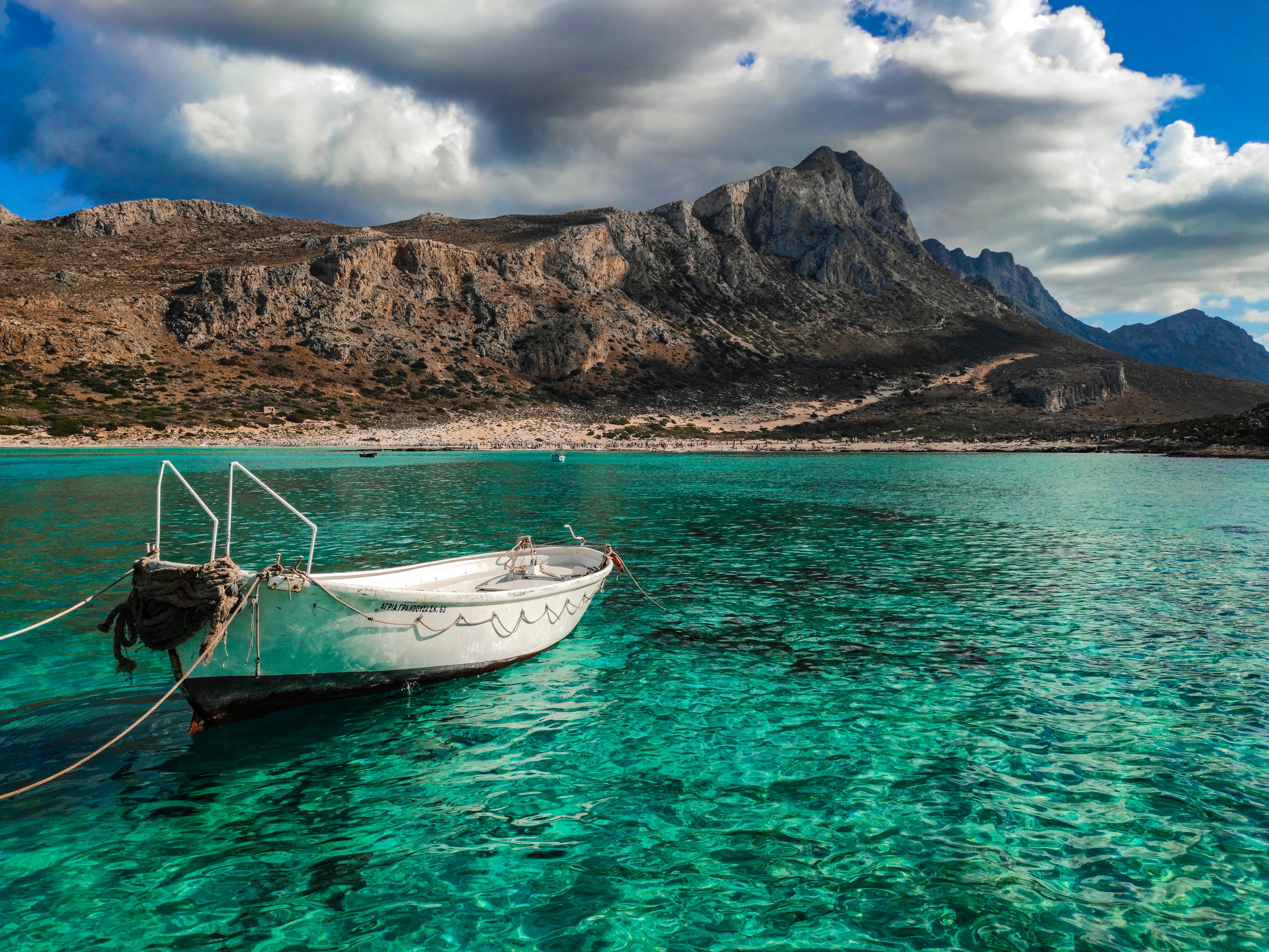 A small white boat moored in the turquoise sea at Crete, Greece, with mountains in the background