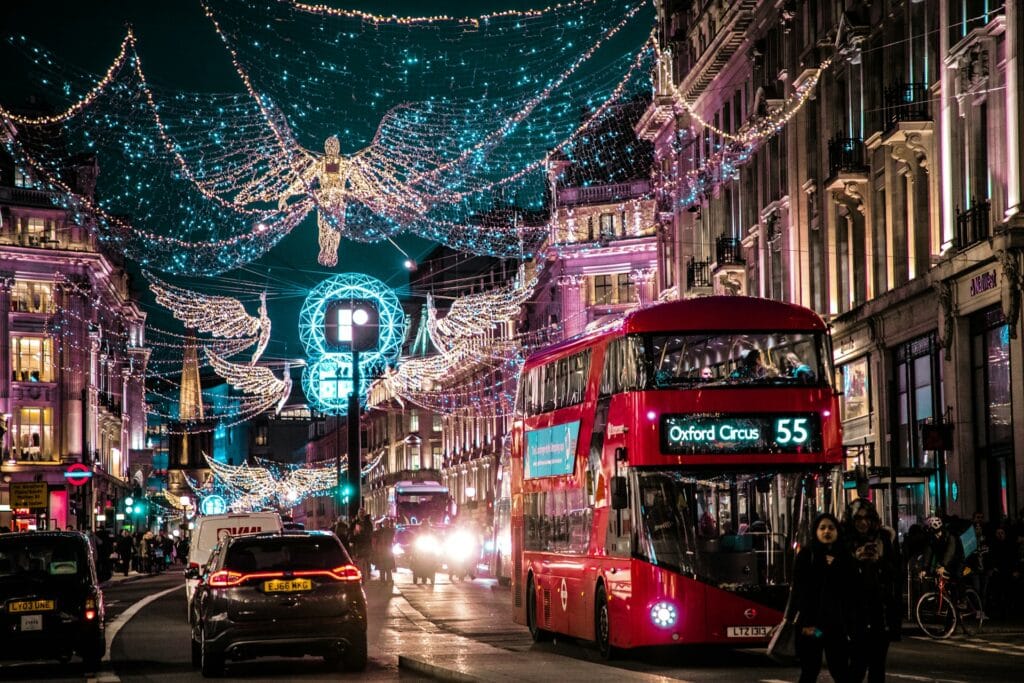Red double-decker bus driving beneath glowing Christmas angel light displays on a London street.