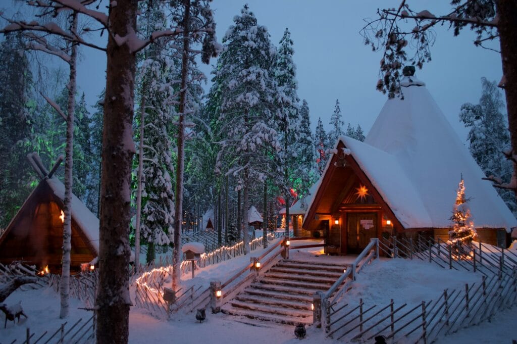 Snow-covered wooden cabin lit up with warm Christmas lights in the Arctic forest of Rovaniemi, Finland.